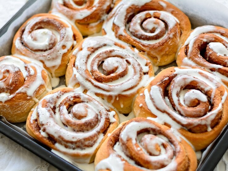 9 Bananen-Zimtschnecken auf einem Blech mit Backpapier, verziert mit Zuckerguss.