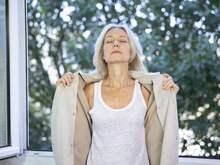 Frau mit Hitzewallungen steht am Fenster