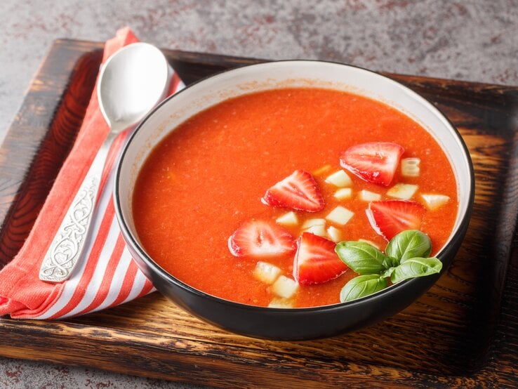 Tomaten-Erdbeer-Gazpacho in Schwarzer Suppenschüssel auf Holzbrett.