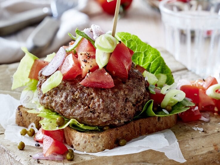 Leichter Beef-Burger mit grünem Pfeffer auf Holzunterlage, im Hintergrund Geschirr.