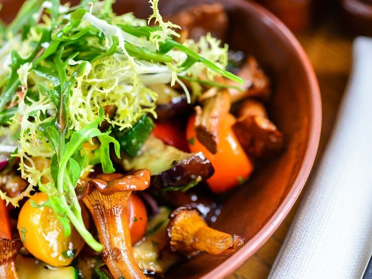 Eine braune Schale mit dem Salat auf einem dunklen Holztisch sehr nah dran fotografiert.