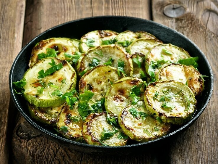 Draufsicht: Eine Pfanne frittierte Kräuter-Zucchini auf einem Untergrund aus Holz.