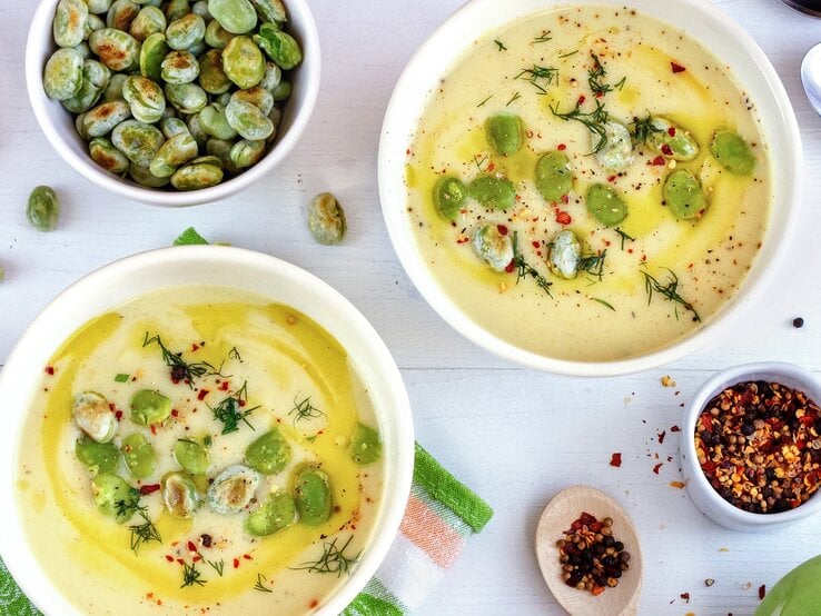 Zwei Suppenteller auf einem weißen Tisch mit Bohnen, Brot, Chilipulver und Kohlrabi.