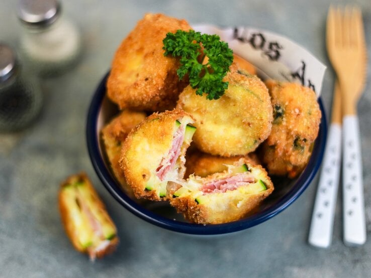 Cordon bleu mit Zucchini, Mozzarella und Schinken, angeschnitten serviert in einer großen Schale und garniert mit frischer Petersilie. 