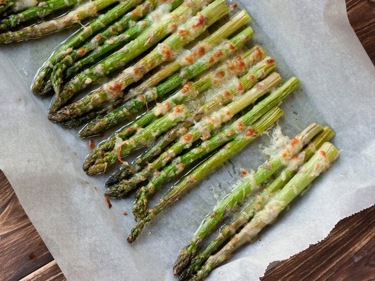 Überbackener Spargel aus dem Ofen auf einem mit Backpapier belegten Blech. Das Ganze auf einem hölzernen Untergrund.