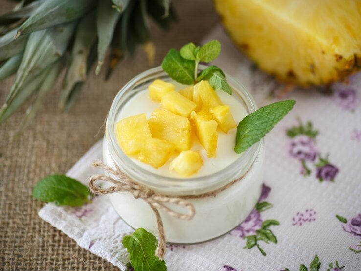 Quark-Dessert mit Ananas im Glas. Angerichtet ist das Ganze auf einem braunen Leinentuch.