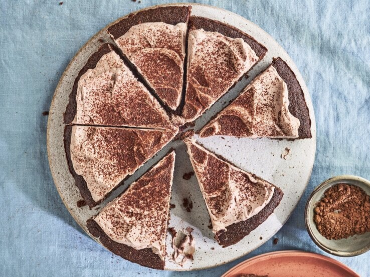 Auf einem Teller liegt ein Keto-Schokoladenkuchen. Er ist mit Kakaopulver bestreut.