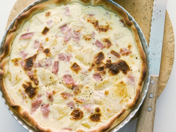 In einer runden Form ist eine Quiche Hawaii angerichtet. Sie ist mit Schinken und Ananas zubereitet.