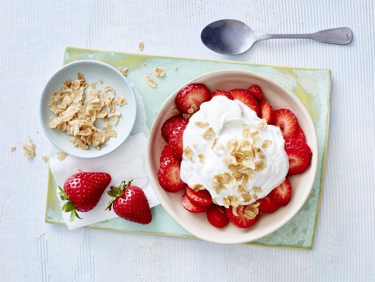 In einer Schüssel sind Erdbeeren mit Vanillequark angerichtet. Darüber sind Dinkel-Flocken gegeben. 