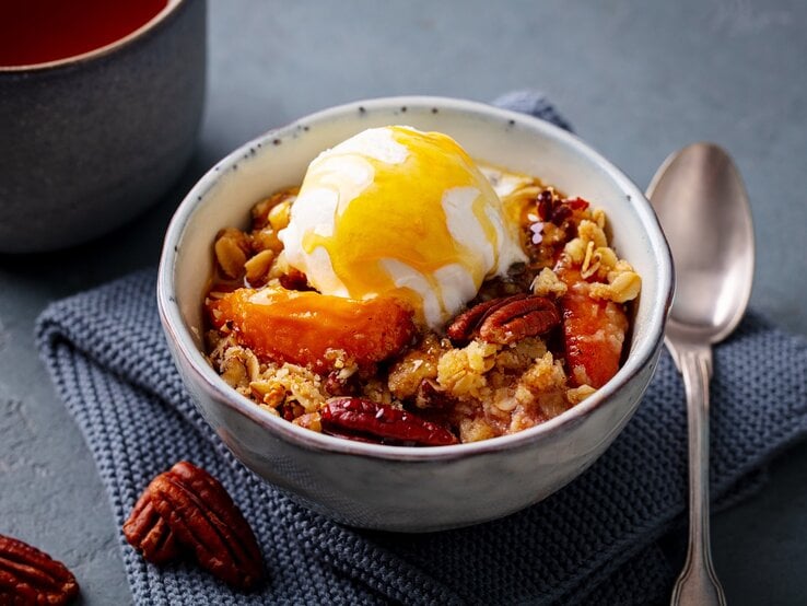 Eine Schale mit Pfirsich-Crumble auf einem grauen Küchentuch.