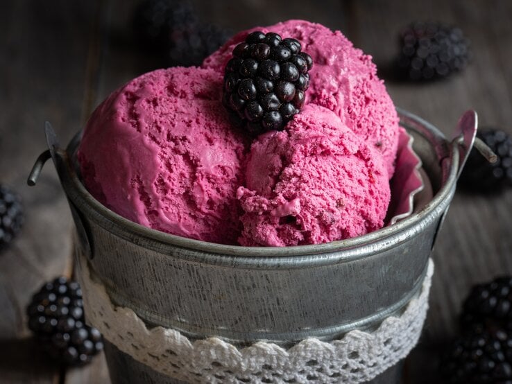 Ein kleiner Metalleimer mit 3 Kugeln Brombeer-Bananen-Eis, garniert mit einer Brombeere, dunkle Umgebung.