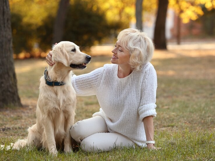 Reife Frau sitzt neben ihrem Hund und streichelt seinen Kopf.