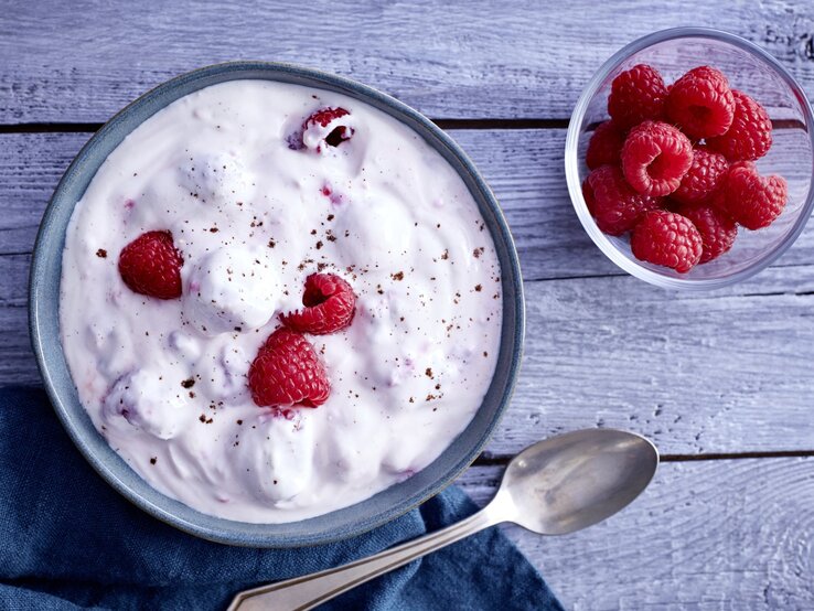Himbeer-Traum in einer Schale, bestehend aus  Zitronenabrieb, Himbeeren, Honig und griechischem Joghurt, serviert auf einem hölzernen Frühstückstisch. 