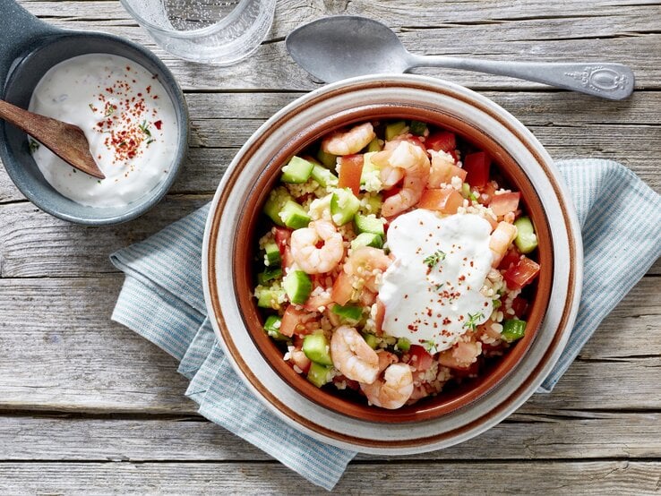 Bulgur-Salat mit Garnelen, Tomaten, Gurken und frischem Joghurt-Dip, serviert auf einem rustikalen Holztisch, von oben fotografiert. 