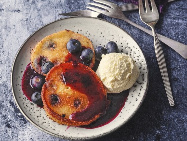Auf einem Teller liegt eine Portion Siegerländer Blaubeer-Pfannkuchen mit Eiscreme und Soße. 