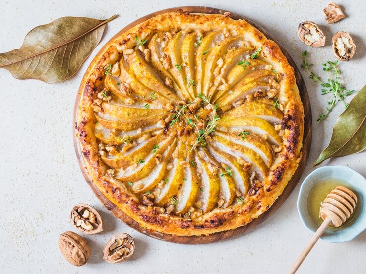 Walnuss-Birnentarte mit Blätterteig mit herbstlicher Dekoration auf weißem Untergrund.  | © Getty Images/leonori