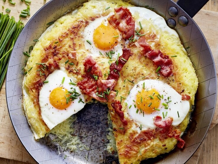 Auf einem Teller liegen Rösti mit Spiegelei. Die sind mit Schnittlauch garniert. 