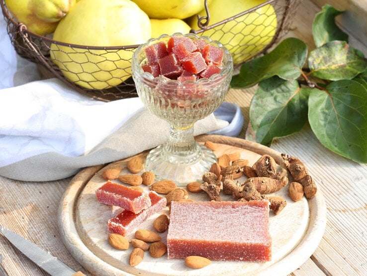 Quittenbrot am Stück und in Würfel geschnitten / Holzbrettchen / frische Quitten / Untergrund Holz / Draufsicht schräg