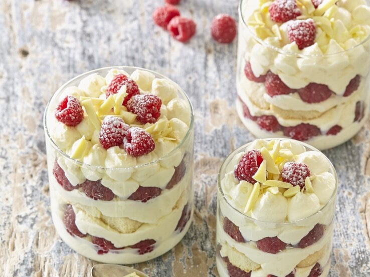 Drei kleine Gläser mit Himbeer-Tiramisu. Das Ganze auf einem hölzernen Untergrund. 