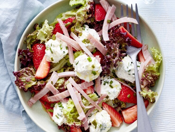 Sommersalat mit Erdbeeren, Frischkäse und Schinken in einer weißen Schale. Darin liegt eine Gabel. 
