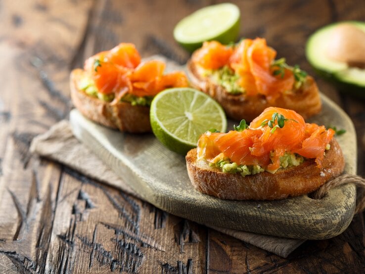 Drei Lachs-Bruschetta mit Avocado auf einem Holztablett. | © Shutterstock/MariaKovaleva