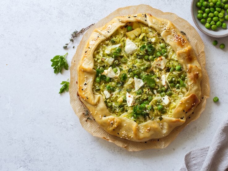 Galette gefüllt mit Kartoffeln, Wirsing und Erbsen, überbacken mit Feta Käse, vor einem hellgrauen Hintergrund von oben.