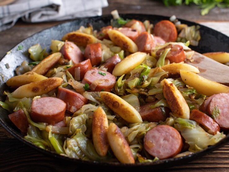 Eine gusseiserne schwarze Pfanne mit dem Schupfnudel-Gericht auf einem Holztisch.