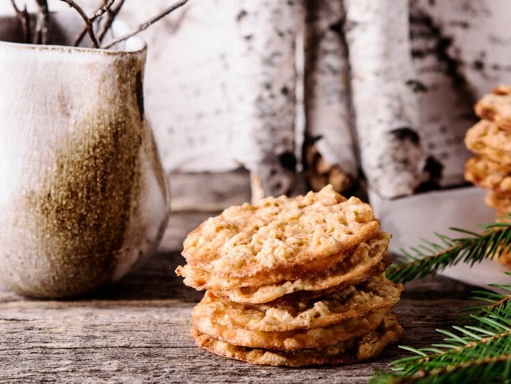 Haferkekse auf einem Holztisch mit einer weißen Vase, Birken und Tanne im Hintergrund. | © Shutterstock/ Trendy Rowdy