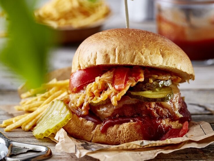 Camping-Burger auf Papier mit Kartoffel-Sticks im Hintergrund auf Holzuntergrund. 