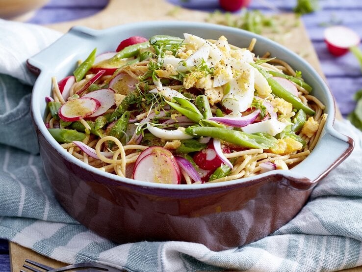 Eine Schüssel Bohnen-Nudel-Salat mit Eiern steht auf einem blau-weißem Tuch. Im Hintergrund sieht man Radieschen. | © EAT CLUB / Isabell Triemer