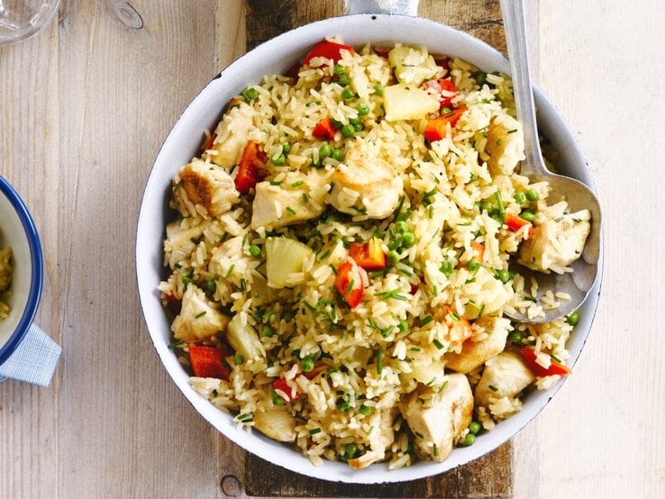 In einer Schüssel ist ein Reissalat mit Huhn, Ananas und Tomaten angerichtet. Er ist mit Schnittlauch überstreut.