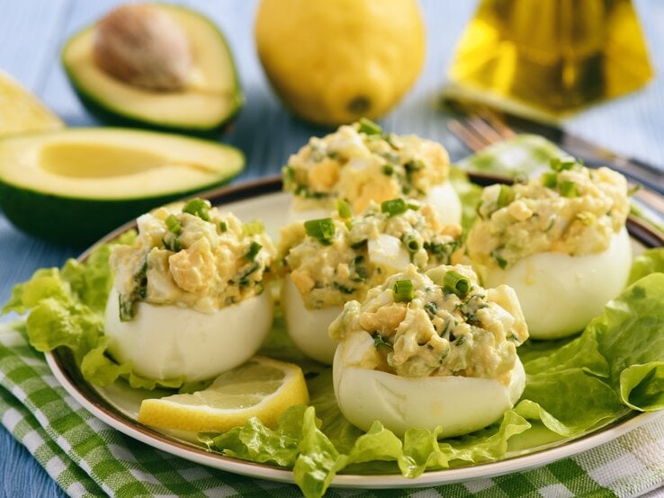 Gefüllte Eier mit Avocado auf Salatblättern umrundet von den Zutaten.