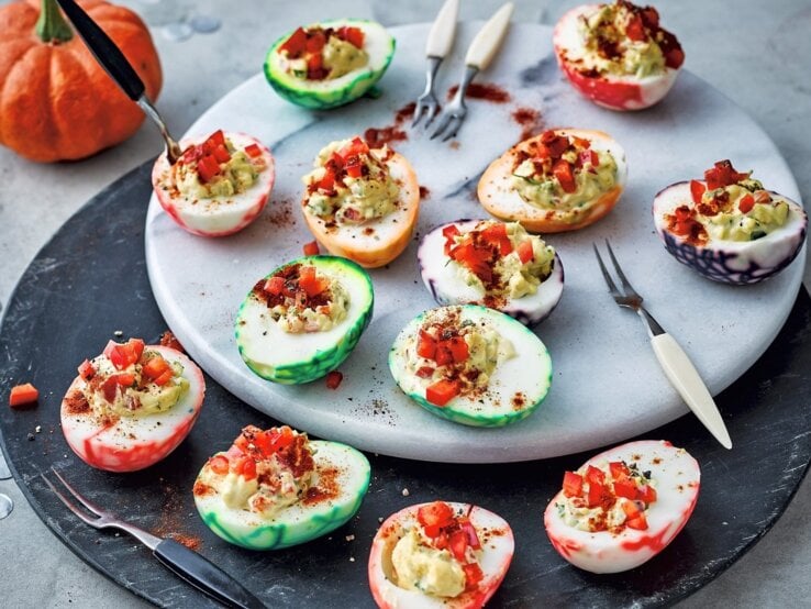 Auf einem Teller liegen gefüllte Halloween-Eier. Sie sind mit Paprika verfeinert.