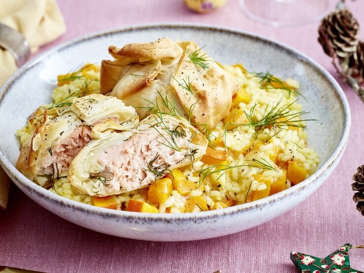 Lachs-Päckchen auf Kürbis-Risotto auf grauem Teller und rosa Tischdecke. Daneben Serviette und Dekoration. Draufsicht. | © EAT CLUB / Isabell Triemer