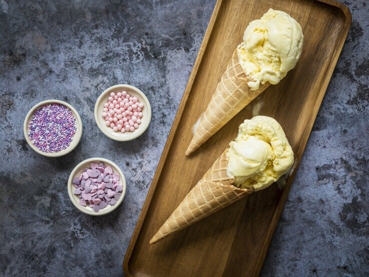 Eiscreme in Waffeln auf einem kleinen Holzbrett mit bunten Zuckerperlen auf einem dunklen Steintisch. | © GettyImages/ Anthia Cumming