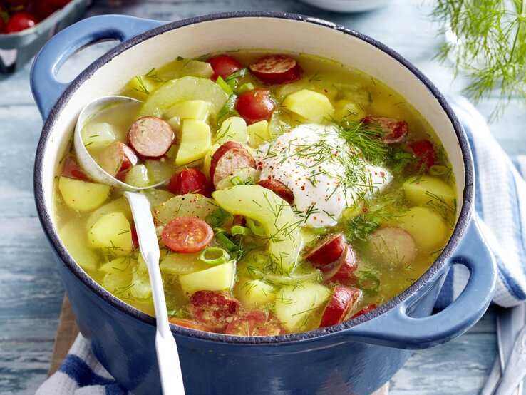 In einem Topf ist eine Portion Schmorgurken-Kabanossi-Eintopf angerichtet. Sie ist mit Dill und saurer Sauce serviert. 