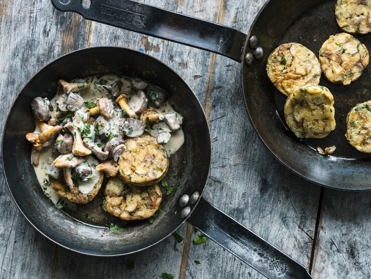 Auf einem Teller ist eine Portion bayerisches Pilzragout mit Brezenknödeln angerichtet. Daneben steht eine Pfanne mit weiteren Knödeln. 