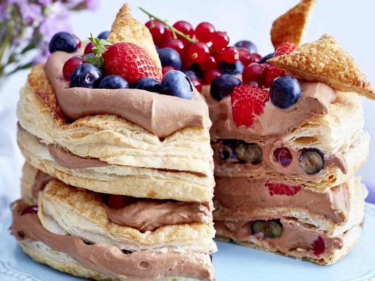 Auf einem Teller steht eine Schoko-Beeren-Torte. Sie hat mehrere Schichten Creme und ist mit verschiedenen Beeren dekoriert. | © EAT CLUB / Isabell Triemer