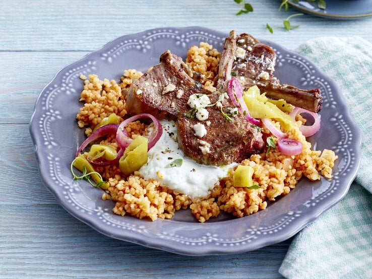 Griechische Koteletts vom Lamm auf Bulgur auf einem schön verzierten Teller der auf einem Untergrund aus Holz steht.