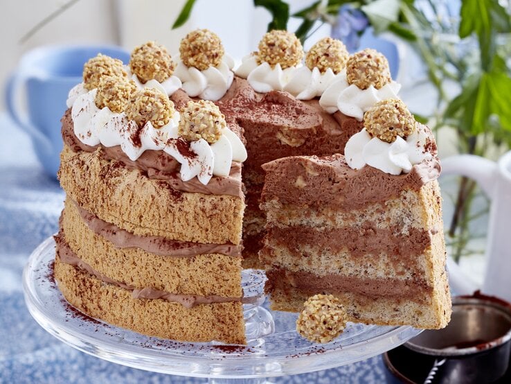 Auf einem Tortenhalter steht eine Giotto-Nusstorte. Sie ist angeschnitten. Man erkennt die cremige Füllung. Sie ist dekoriert mit Sahne und Giotto-Kugeln.  | © EAT CLUB/Isabell Triemer