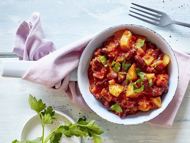 Kartoffel-Bohnen-Pfanne auf einem weißen Teller. Das Ganze auf einem blauen Untergrund. 