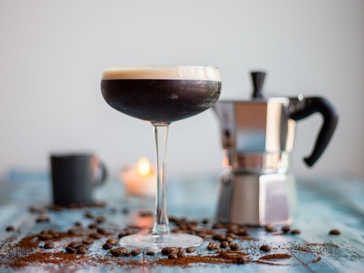 Ein Espresso Martini sowie eine Espressokanne, Kaffeebohnen und eine Kerze.