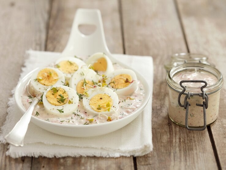 Die gekochten und halbierten Eier in Merrettichsauce auf einem weißen Teller und dunklem Holztisch.