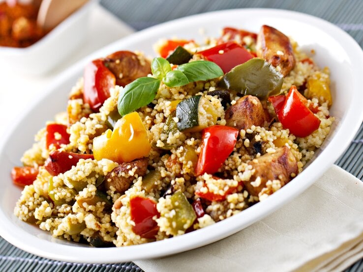 Weißer Teller, darauf Couscous-Salat mit Gemüse und Hähnchen.