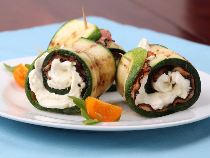 Zucchini-Schinken-Röllchen mit Mozzarella auf weißem Teller.  | © iStock/ IngridHS 