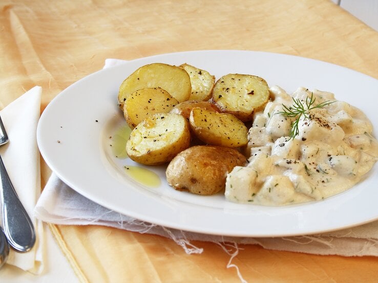 gebratener Kohlrabi neben einer hellen Soße auf einem weißen Teller vor rustikalem Ambiente. 