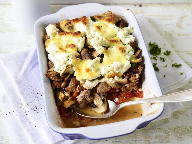 Eine weiße Auflaufform mit dem Gericht auf einem rustikalen, hellen Holztisch. | © StockFood / Arras, Klaus