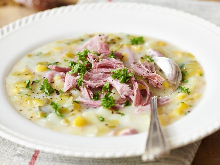 Runder verzierter Teller mit einer Lauch-Mais-Suppe, garniert mit Schinken. 