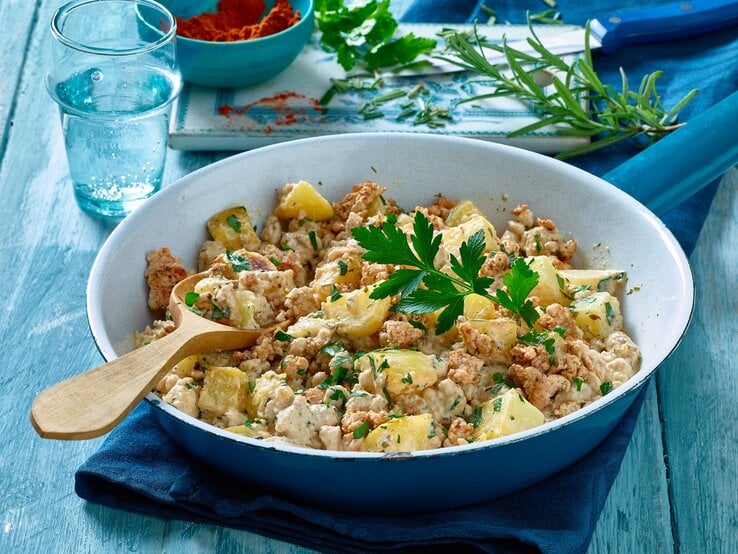 Kartoffel-Hack-Pfanne in einer blau-weißen-Schüssel auf einem blauen Geschirrtuch auf einem blauen Tisch. Hinten auf dem Bild ein Schneidebrett.  | © Matthias Liebich