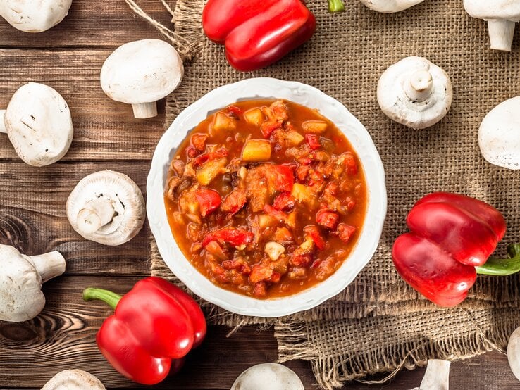 Ungarischer Eintopf mit Hackfleisch & Paprika auf rundem Teller, der auf einem Holztisch steht.